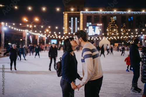 Young couple skates at the rink, kisses and holds hands.