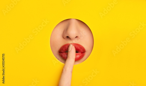 Girl with red lips showing hush sign, closing lips with finger photo