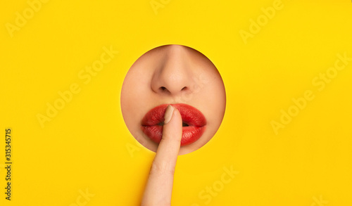 Girl with red lips showing hush sign, closing lips with finger
