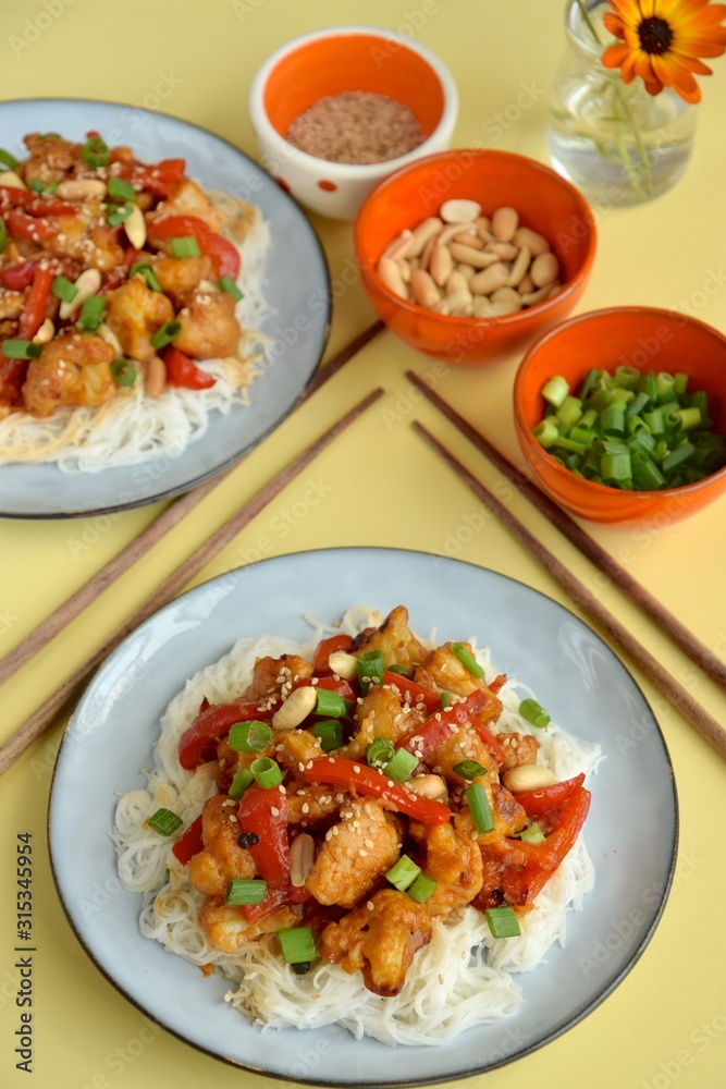 Cauliflower Kung Pao with bell pepper and rice noodles. Garnish with peanuts, scallions and sesame seeds. Vegan food