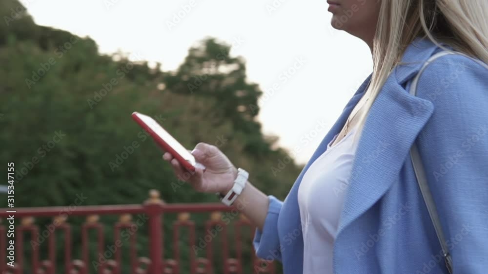 A beautiful woman in stylish clothes walks on a pedestrian bridge in a big city and uses the phone A beautiful woman in stylish clothes walks on a pedestrian bridge in a big city and uses the phone