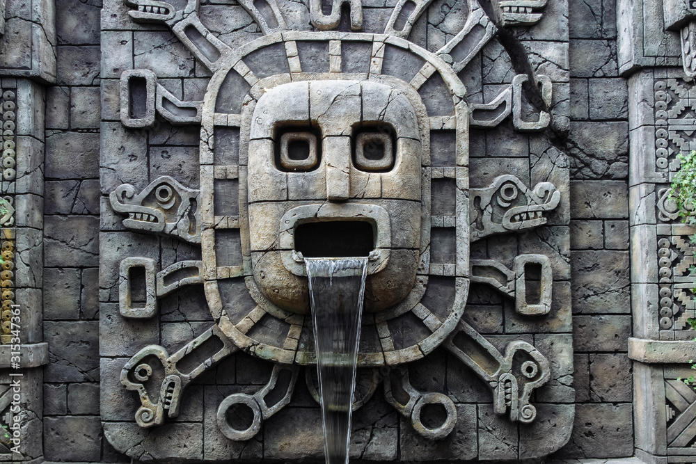 Waterfall in a stone wall and a sculpture of ancient Mayans with
