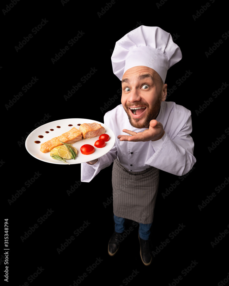 Funny Chef Guy Holding Fish Dish Standing In Studio, High-Angle Funny Chef Guy Holding Fish Dish Standing In Studio, High-Angle