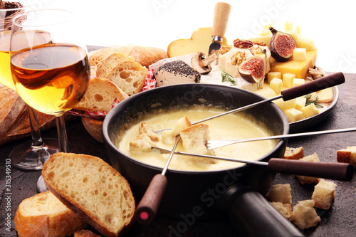 Gourmet Swiss fondue dinner on a winter evening with assorted cheeses on a board alongside a heated pot of cheese fondue with two forks dipping