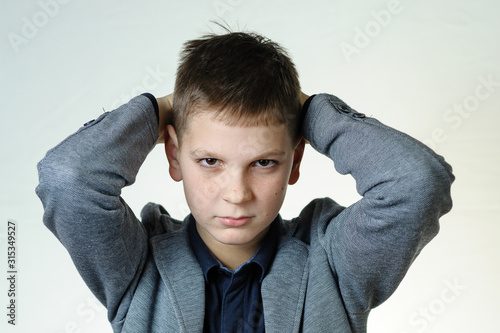 Portrait of a teenage boy on a gray background, close-up, hands behind his head, stubbornly looking at the camera photo