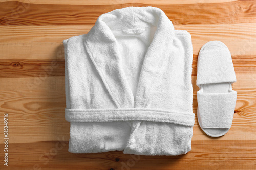 Clean folded bathrobe and slippers on wooden background, flat lay
