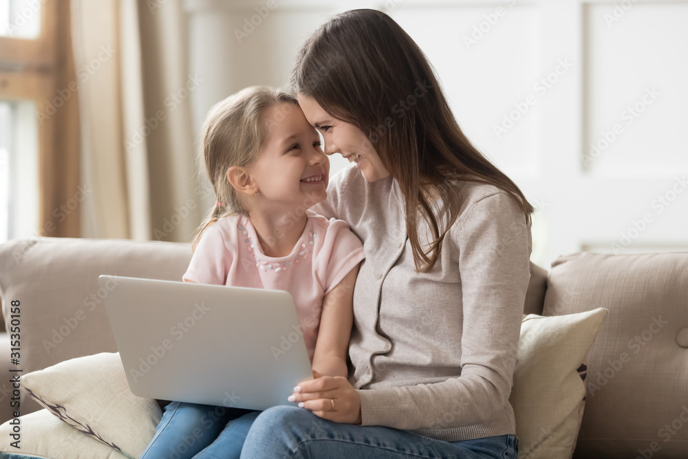 Loving young mother and little daughter touching foreheads, using laptop Loving young mother and little daughter touching foreheads, using laptop