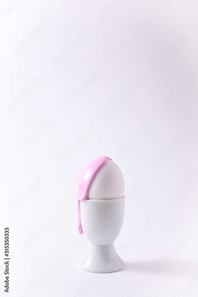 Easter egg with liquid paint on it. Minimalism concept. Pink pastel colour on white background
