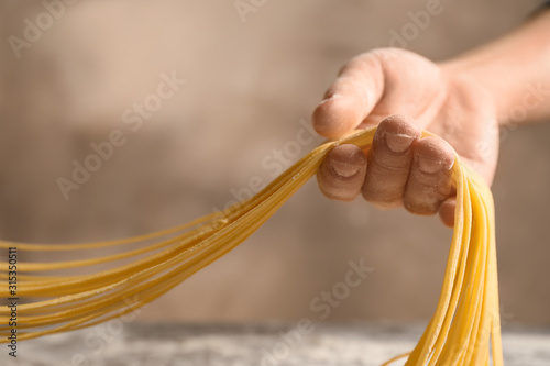 Woman holding noodles on light brown background, closeup. Italian pasta