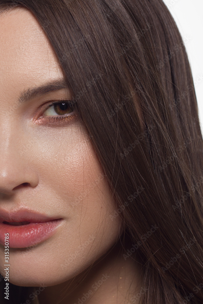 Obraz premium Close-up half face of sexy european young woman model with classic glamour make-up and nude lipstick. Dark long hairstyle, christmas makeup, dark eyeshadows, natural pink lips with gloss