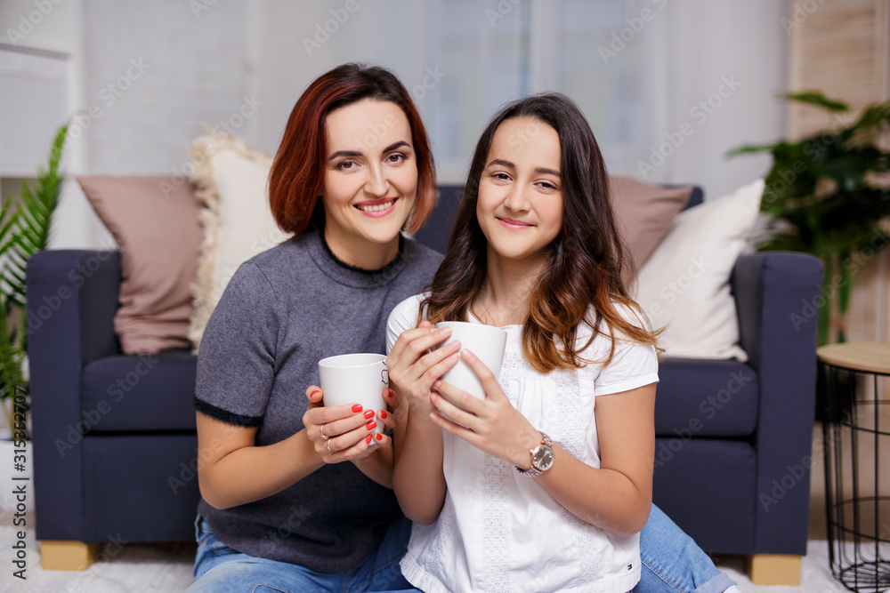 family and home concept - portrait of mother and daughter sitting in living room and drinking tea family and home concept - portrait of mother and daughter sitting in living room and drinking tea