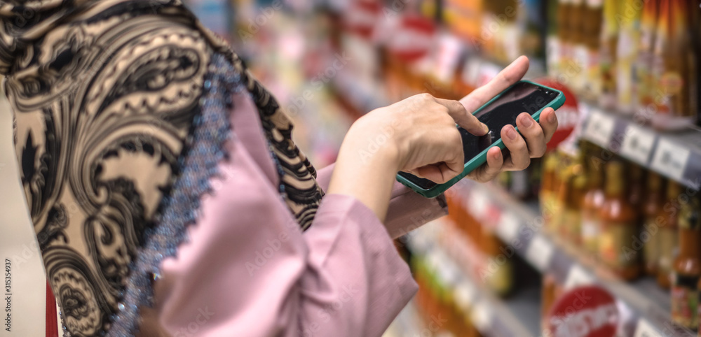 Fototapeta premium Close up of woman hand using smartphone in shopping at supermarket