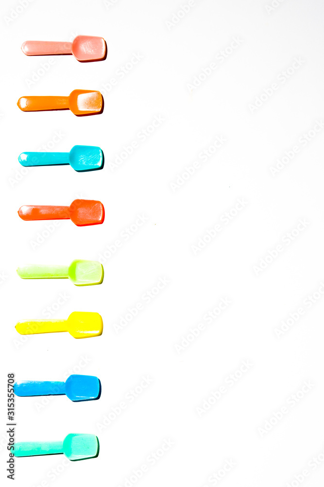 Colored Small plastic ice cream spoon are lined up on a white background, top view Colored Small plastic ice cream spoon are lined up on a white background, top view