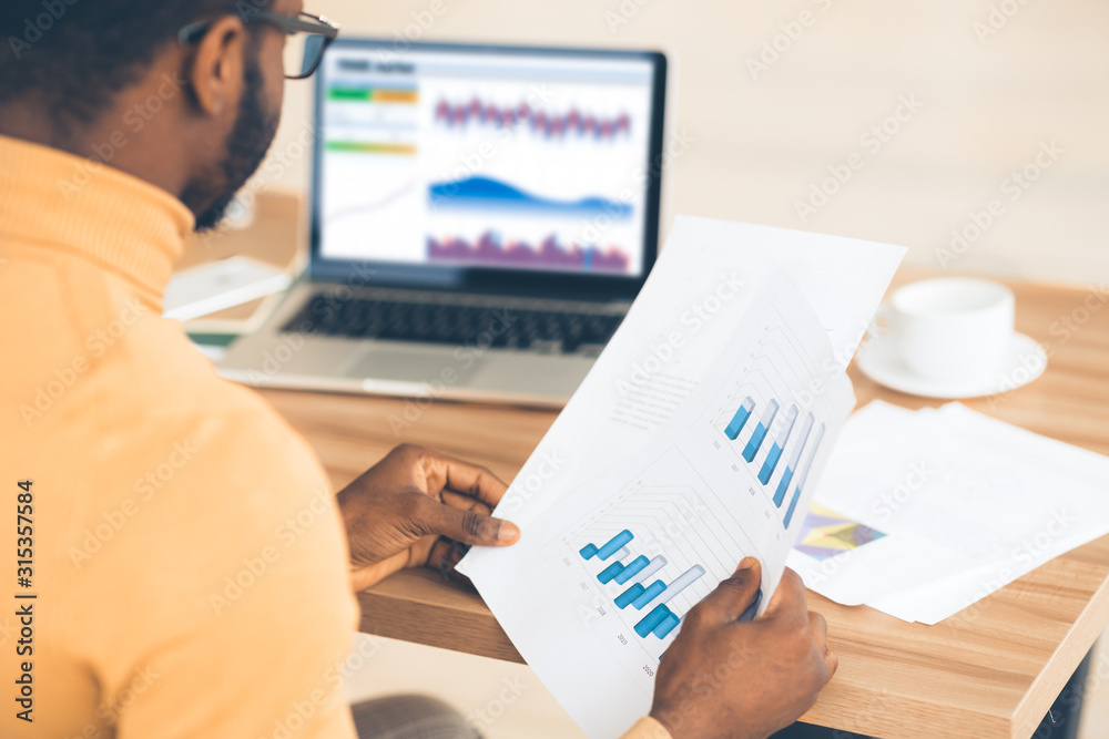 Black manager working with diagrams on pc and paper Black manager working with diagrams on pc and paper
