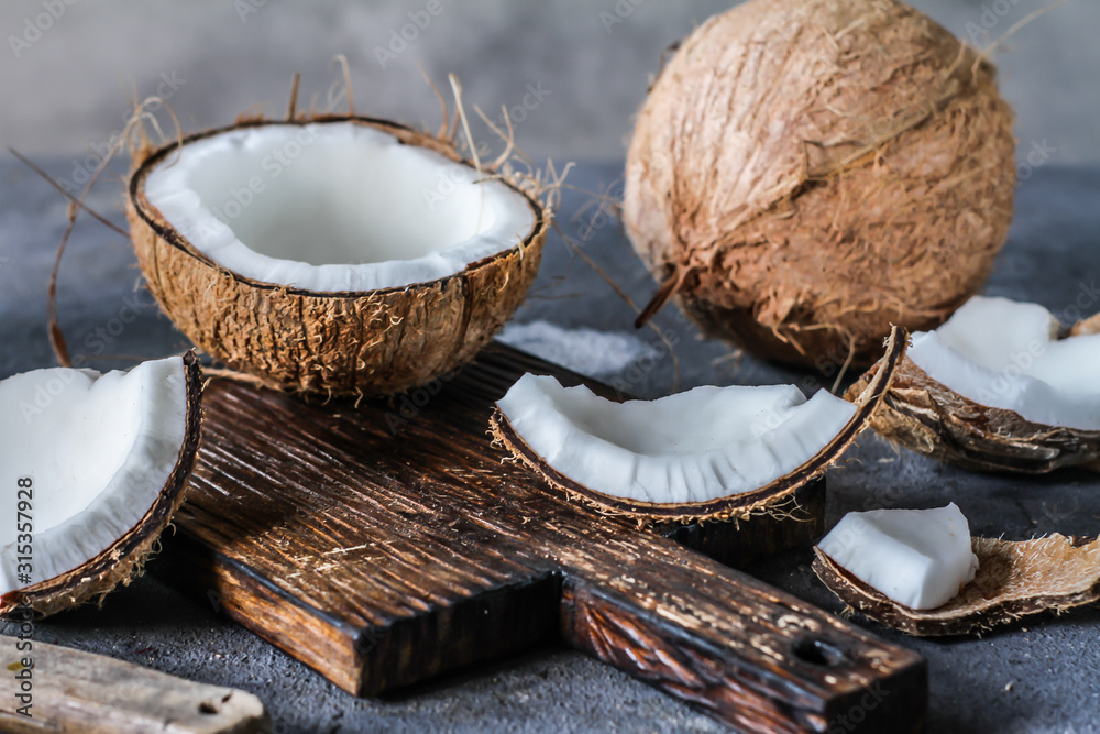 Photo of fresh coconut on a table. Tropical palm fruits. Coconut cut in half. Beach fruit. Retro dark background. Rustic wooden board. Front view. Image