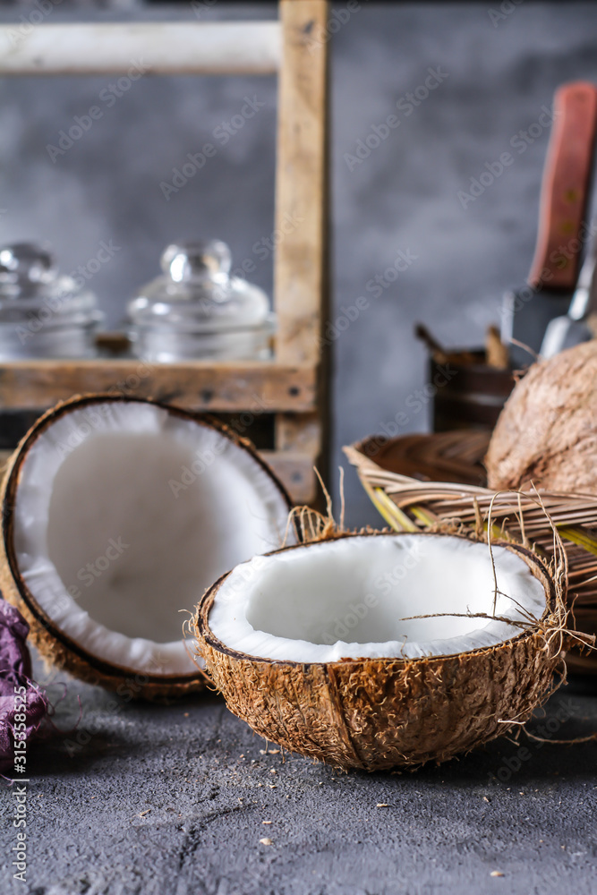 Photo of fresh coconut on a table. Tropical palm fruits. Coconut cut in half. Beach fruit. Retro dark background. Rustic wooden board. Front view. Image