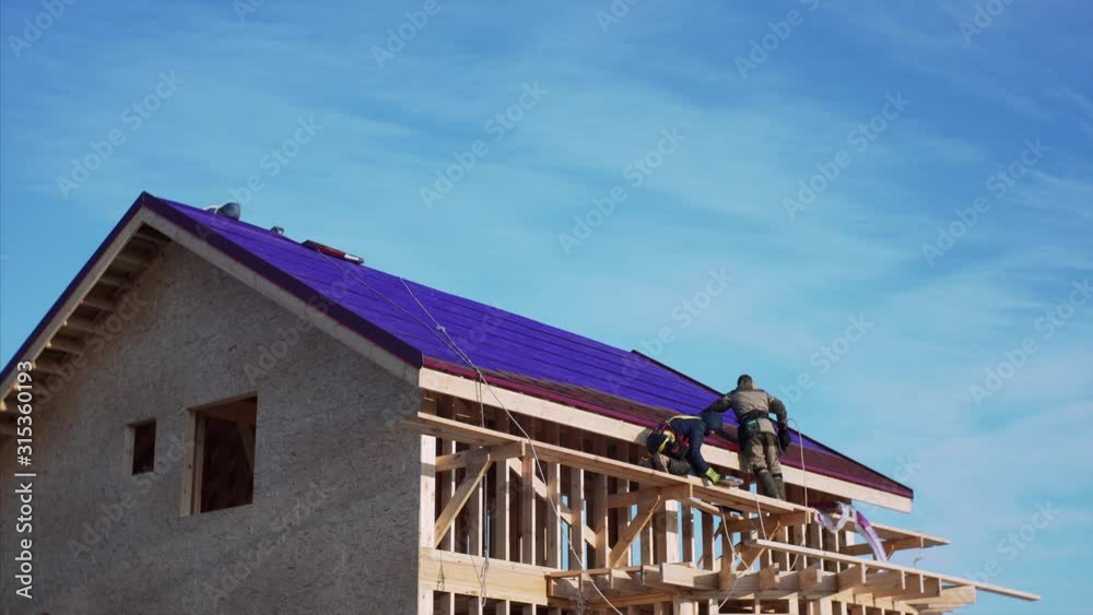 Timelapse of frame house under construction. Builders in safety harness are covering the roof with soft tiles Timelapse of frame house under construction. Builders in safety harness are covering the roof with soft tiles