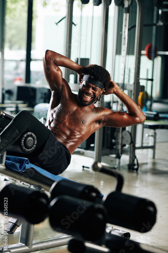 Vertical shot of African American guy working hard on his abs on abdominal bench in gym