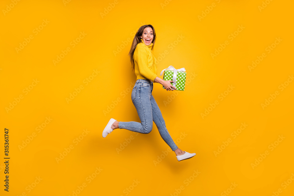 Full length profile side photo of amazed crazy funky girl like holiday sales hold green dotted gift box bring boyfriend jump run wear casual style clothing isolated yellow color background - obrazy, fototapety, plakaty 