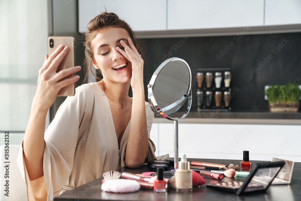 Image of young woman taking selfie photo while applying face makeup Image of young woman taking selfie photo while applying face makeup