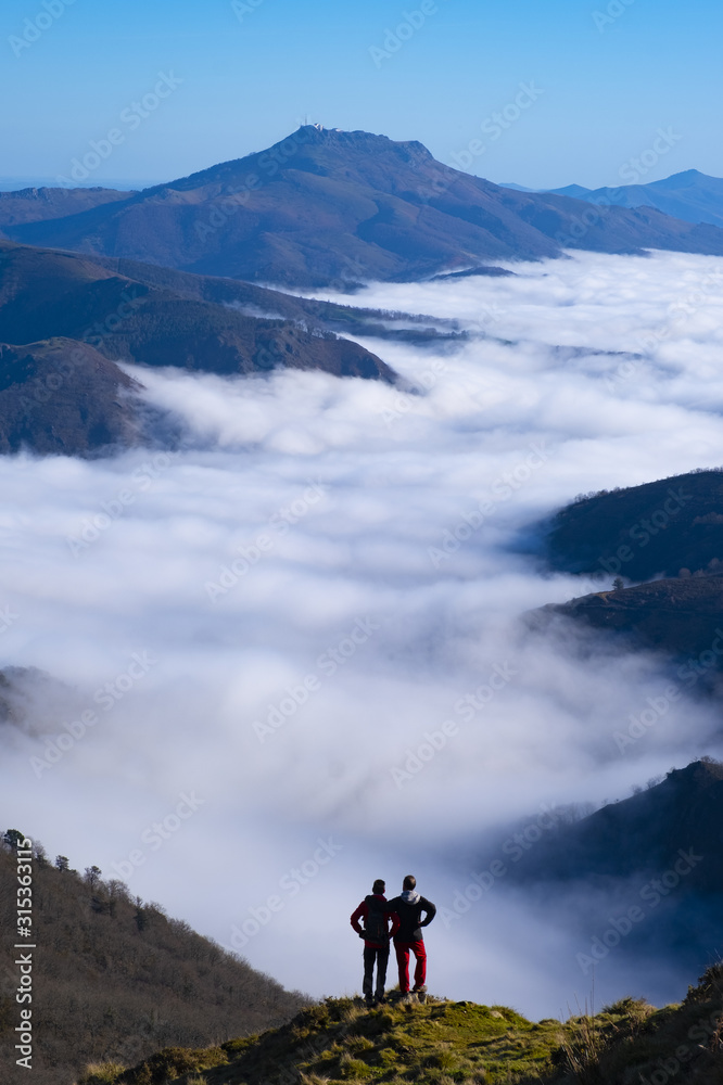 Two mountaineers with sea of clouds and Mount Larun in the background from the natural park of Aiako Harriak, Euskadi Pyrenees