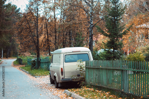 Mini van in the village near the house with a green fence. Wilderness. Natural scenery. Sunny autumn day	