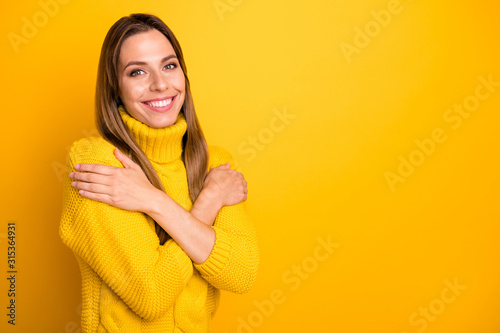 Turned photo of charming content girl hug herself enjoy warm knitted pullover isolated over yellow color background