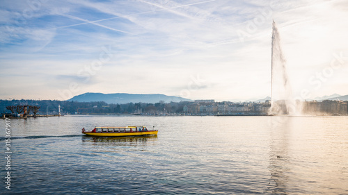 Lake Geneva panorama with the famous Jet d'Eau or water jet and small yellow shuttle boat Geneva Switzerland