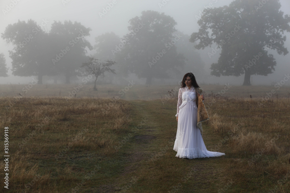 girl in a white dress on a mist field with oaks