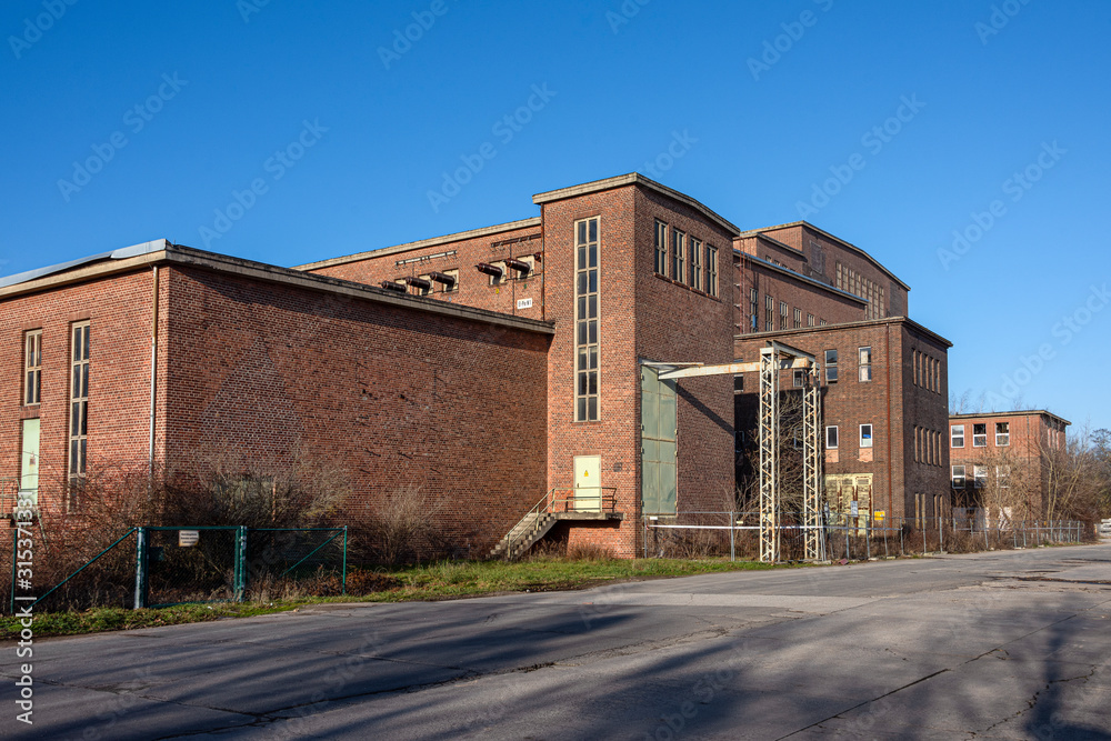 Germany, Saxony-Anhalt, Vockerode: Street view of big old defunct shut down former Vockerode lignite power plant building with brick stone facade, no chimneys and blue sky - concept energy lost place