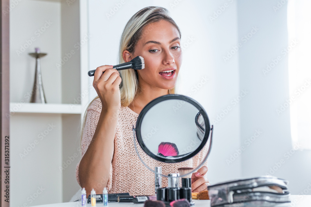 Beauty woman applying makeup. Beautiful girl looking in the mirror and applying cosmetic with a big brush. Girl gets blush on the cheekbones. Powder, rouge