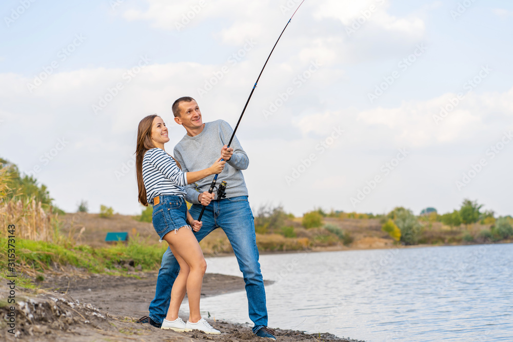 Happy young couple fishing by lakeside a Happy young couple fishing by lakeside a
