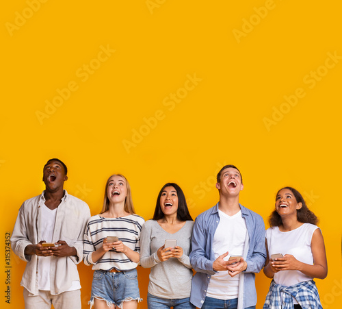 Group of surprised students with smartphones over yellow background photo