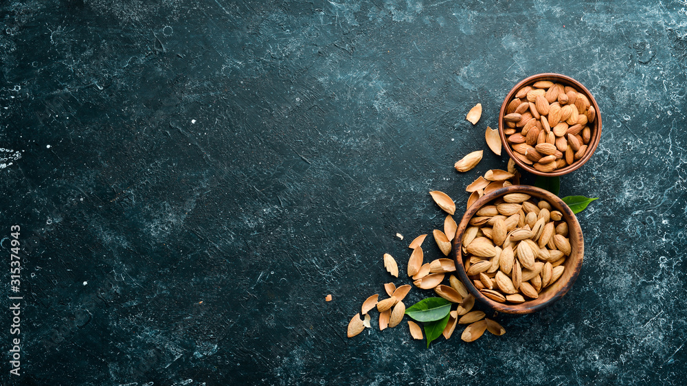 Almond nut in a bowl. Nuts on a black stone background. Top view. Free space for your text. Almond nut in a bowl. Nuts on a black stone background. Top view. Free space for your text.
