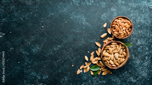 Almond nut in a bowl. Nuts on a black stone background. Top view. Free space for your text.