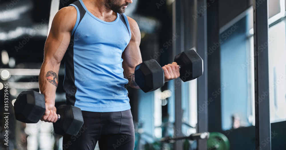 Fototapeta premium Muscular athlete picking up dumbbells at gym