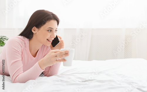 Cheerful girl talking on phone, relaxing with coffee at home on weekends