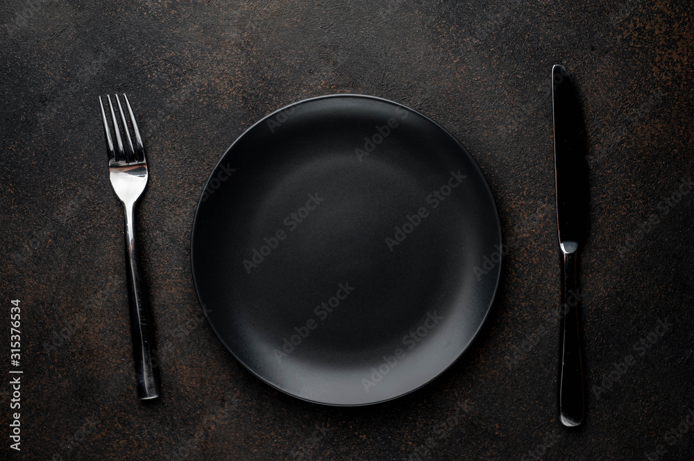 black plate with fork and knife on a stone background black plate with fork and knife on a stone background