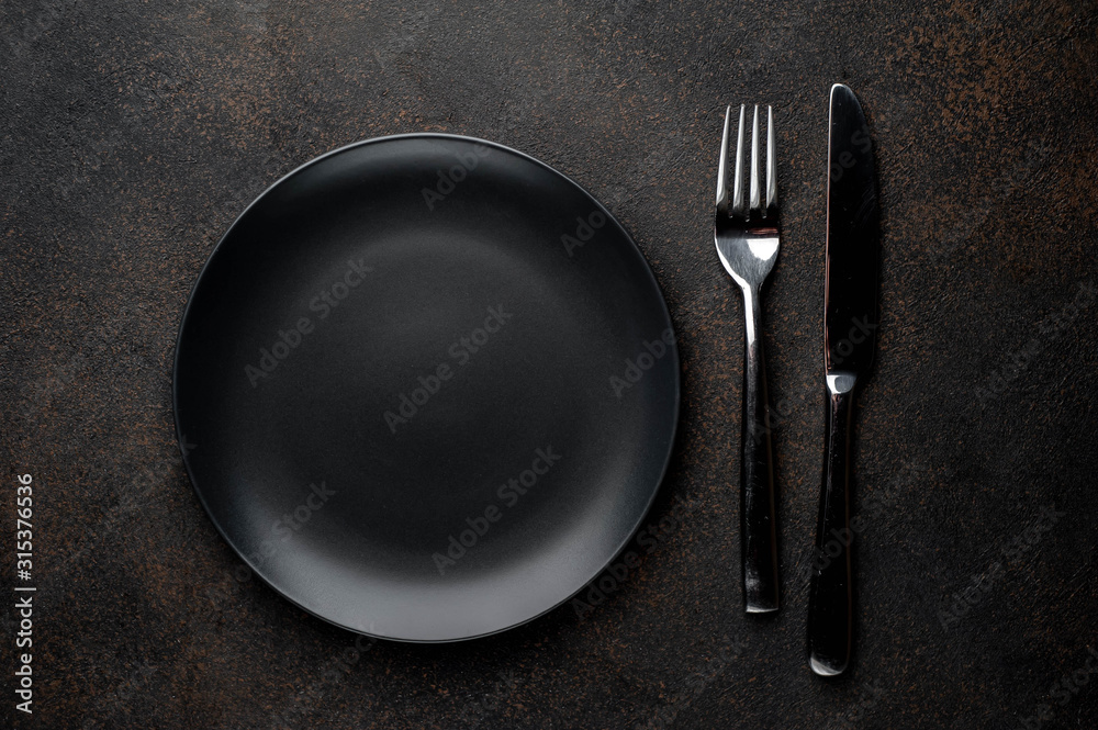 black plate with fork and knife on a stone background black plate with fork and knife on a stone background