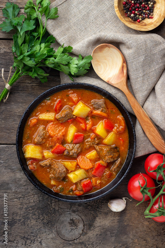 Goulash, beef stew or bogrash soup with meat, vegetables and spices in cast iron pan on wooden table. Hungarian cuisine. Rustic style. Top view.