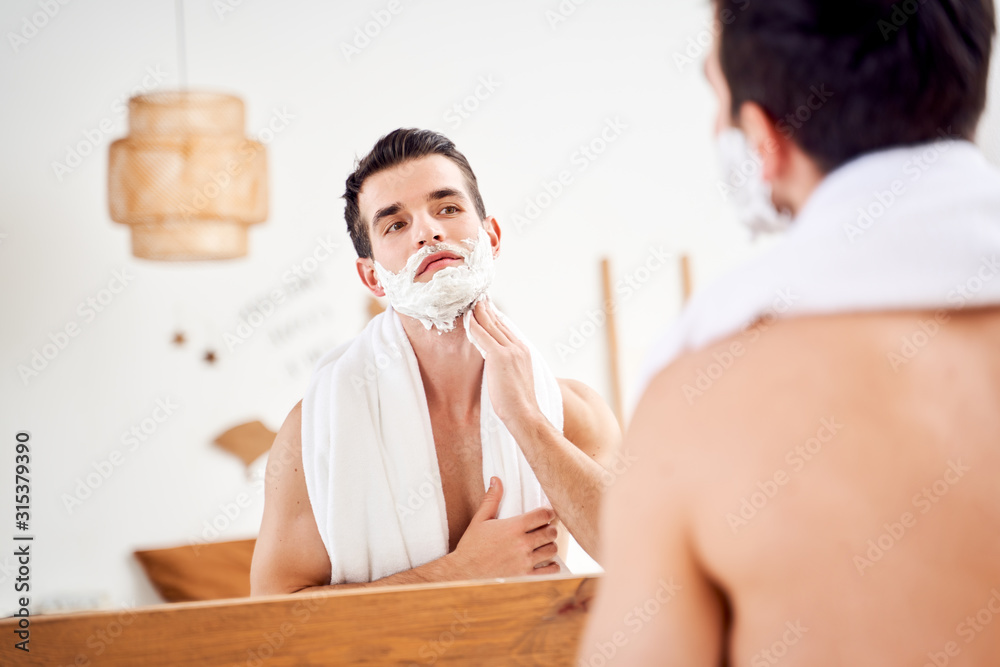 Male with foam on beard near mirror in morning