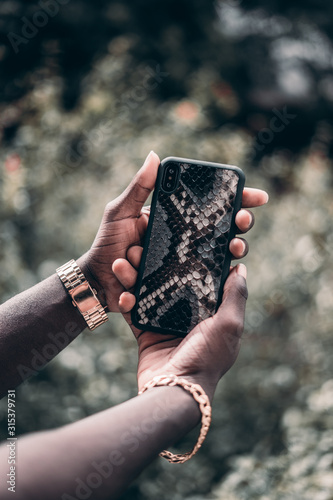 Hand with jewelry hold telephone with case made from snake.