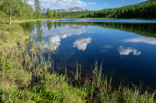 Clouds are reflected in the blue water of a mountain lake. Summer Altai.