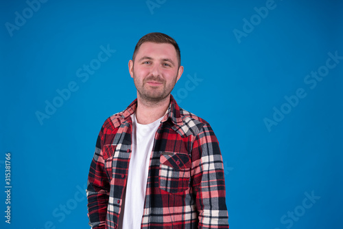 Front view of smiling bearded man in checkered shirt looking at camera isolated on blue background