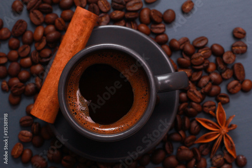 Dark grey cup of coffee, cinnamon and beans on blue table. Hot drink concept. Coffee shop, espresso, top view, closeup