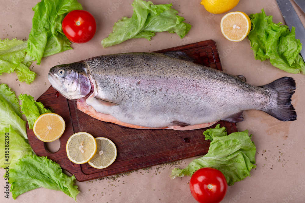 Raw fresh unprepared salmon fish on a wooden board with ingredients for cooking. Lemon, lettuce, tomatoes. Mediterranean cuisine, top view, flat lay. Raw fresh unprepared salmon fish on a wooden board with ingredients for cooking. Lemon, lettuce, tomatoes. Mediterranean cuisine, top view, flat lay.
