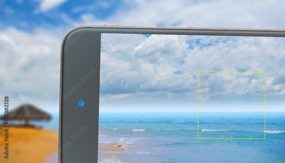 Fototapeta premium Ocean waves against blue sky and palm trees.Blue waves of ocean and yellow sand of beach. Photo smartphone. Smartphone in hand. Landscape on monitor.
