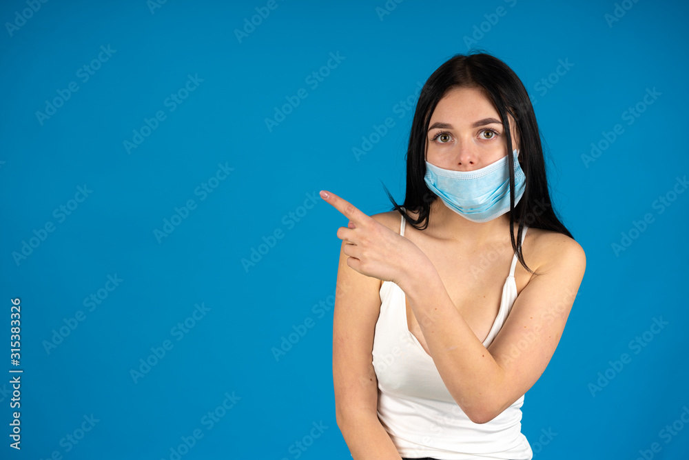 Sick woman in medical mask pointing with finger isolated on blue background Sick woman in medical mask pointing with finger isolated on blue background