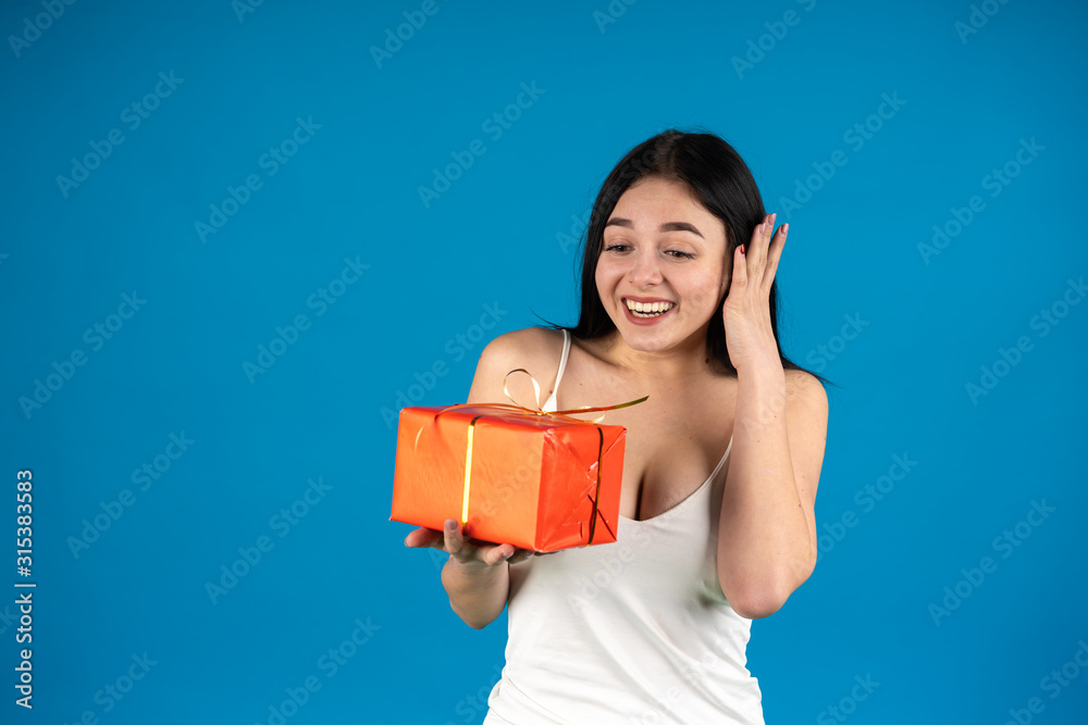 Laughing girl holding birthday gift with ribbon isolated on blue background Laughing girl holding birthday gift with ribbon isolated on blue background