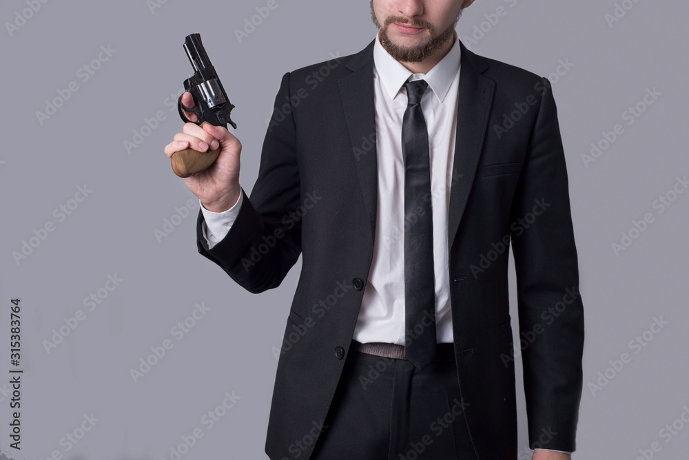 Portrait of a bearded man in a business suit holding a revolver. On a gray background. Portrait of a bearded man in a business suit holding a revolver. On a gray background.